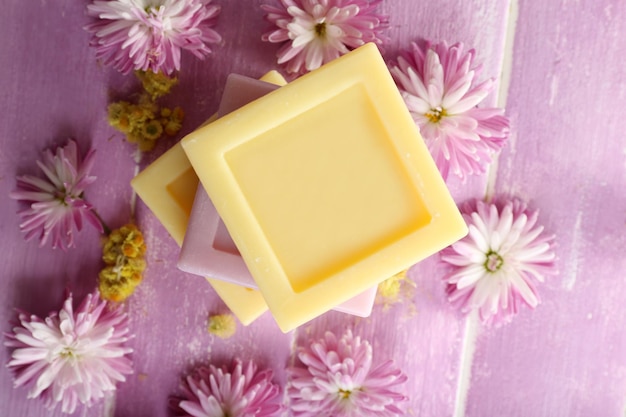 Bars of natural soap and fresh flowers on color wooden background