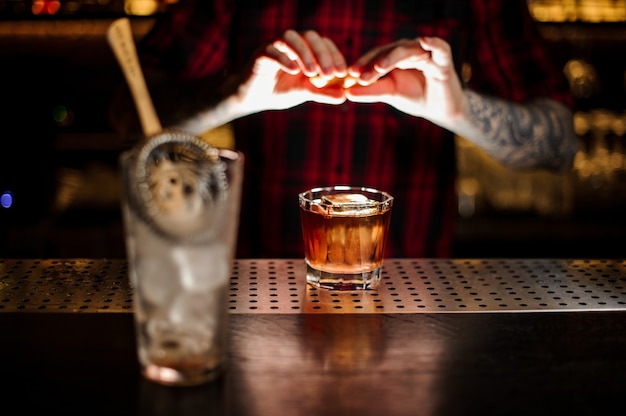 Bartender adding orange zest juice to a Foreign Legion cocktail in the glass on the bar counter