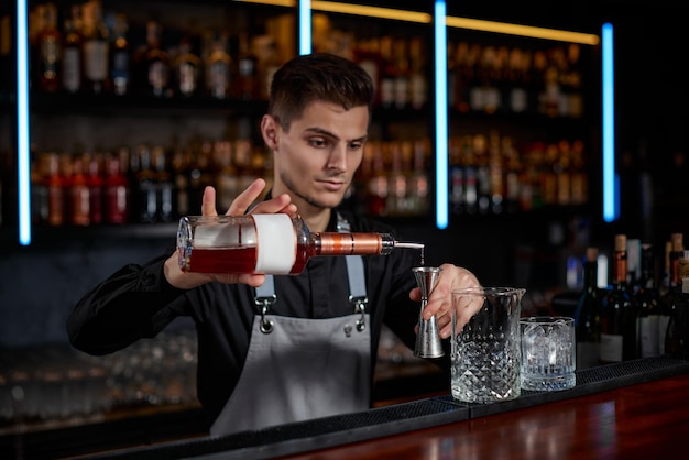 Bartender in apron adds ingredient to glass