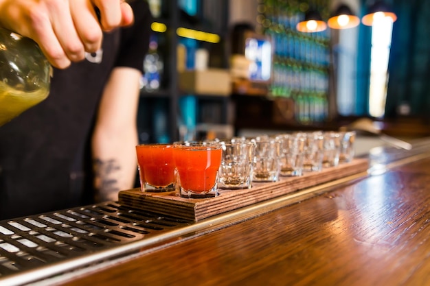 Photo the bartender at the bar pours red tincture into shots horizontal photo