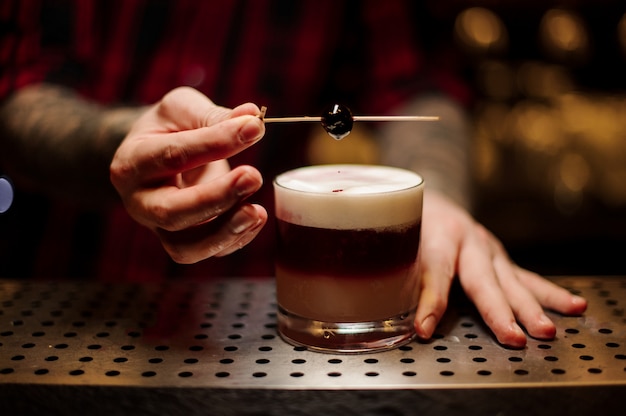 Bartender decorating flaky alcoholic sweet cocktail with a cherry