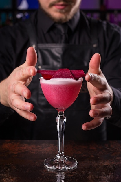 Bartender dressed in black apron and shirt is decorating cocktail drink on black background