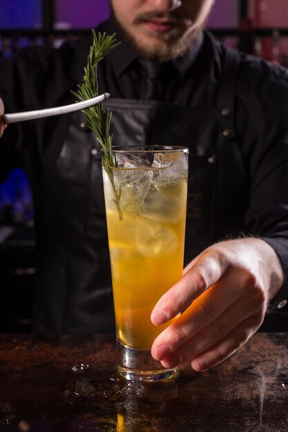 Bartender dressed in black apron and shirt is decorating cocktail drink on black background