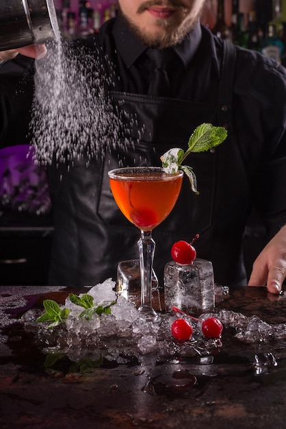 Bartender dressed in black apron and shirt make alcohol cocktail drink on black background