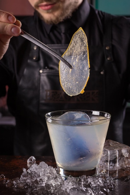 Bartender dressed in black apron and shirt make cocktail drink on black background