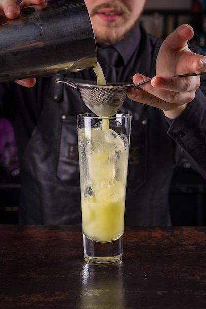 Bartender dressed in black apron and shirt make cocktail lime drink on black background