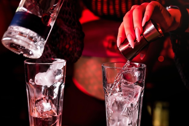 Foto bartender giet alcohol in een glas met ijs met behulp van een jigger het mengen van een alcoholische cocktail in een nachtclub pub restaurant