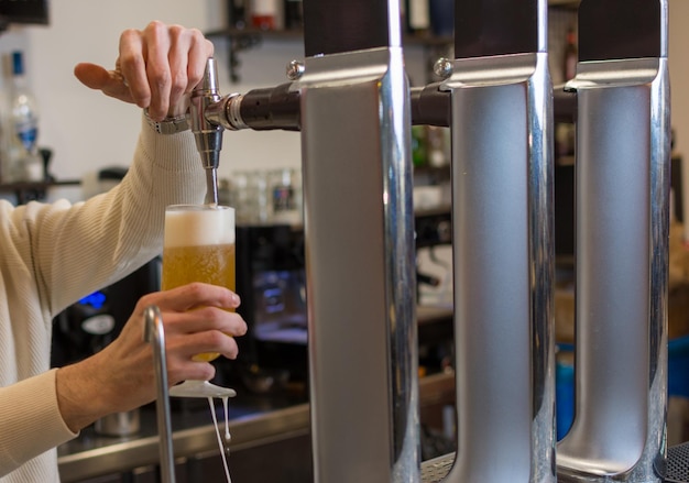 Bartender hand at beer tap pouring a draught beer in glass serving in a bar or pub