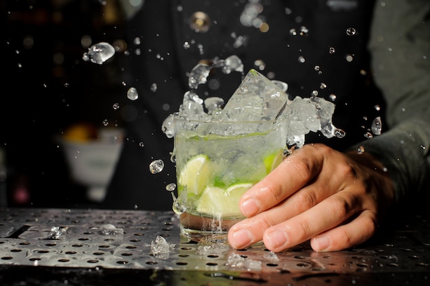 Mano del barista che tiene un bicchiere pieno di cocktail caipirinha