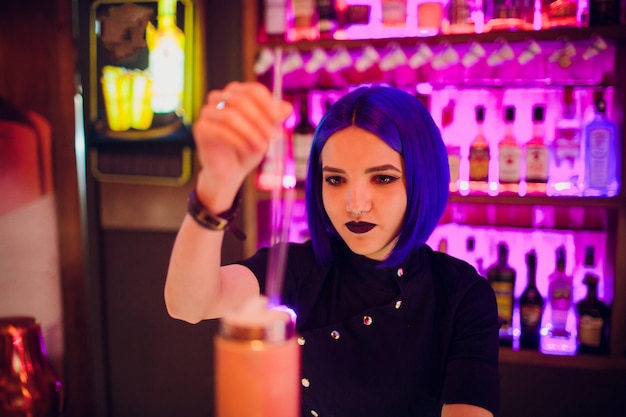 Bartender hand holding a glass with summer light sour cocktail with pink peach liquor decorated with flower under the bar counter