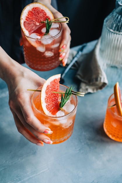 bartender hand holding grapefruit cocktail lemonade glasses  with ice and rosemary.