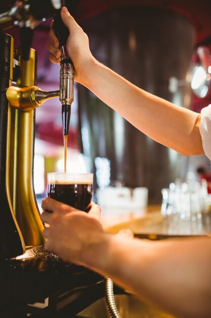 Bartender holding glass below beer dispenser tap