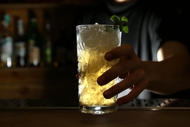 Bartender holding glass of fresh alcoholic cocktail at bar counter closeup