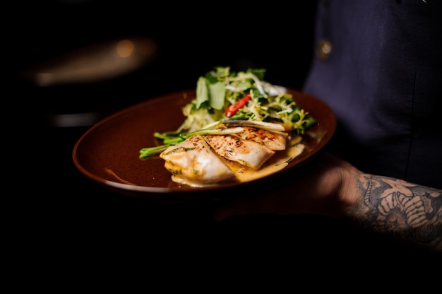 Bartender holding a plate of chicken fillet and salad