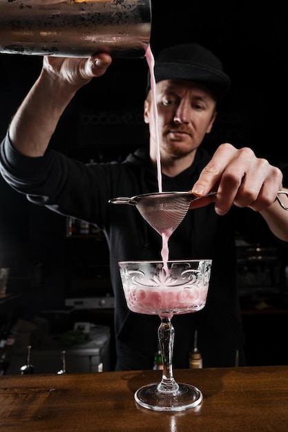 Bartender is pouring pink Clover club alcoholic cocktail in the glass Bartender mixes egg white lemon dry vermouth and gin to prepare the Clover club cocktail