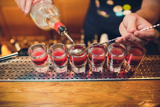 Bartender is pouring tequila into glass against the background of the bar.