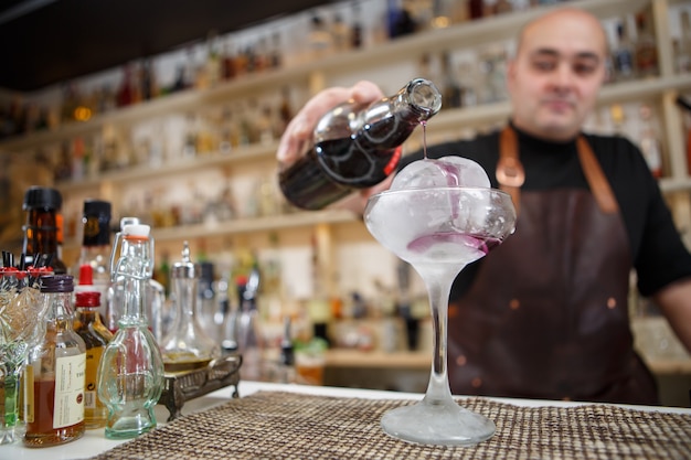 Bartender is pouring wine in the glass with giant ice, wide-angle image.