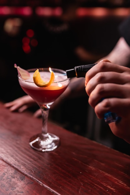 The bartender lights a lemon on an alcoholic cocktail with a\
lighter the bartender prepares drinks for guests night life club\
life great serving of cocktails amazing cocktails