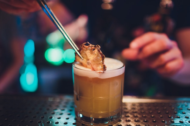 The bartender makes flame over a cocktail with orange peel close up.