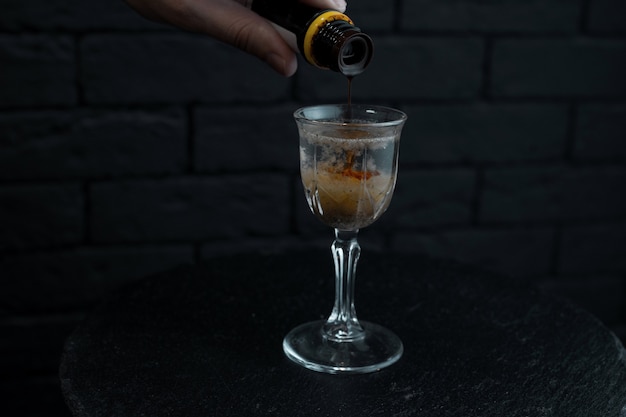 На черном деревянном столе в баре бармен делает необычный сладкий алкогольный напиток из водки и мартини из белого рома с фруктовым сиропом. Вкусный коктейль в винтажном бокале