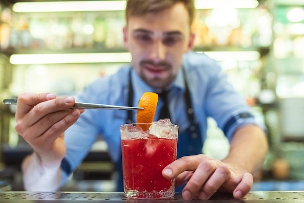 The bartender making a red cocktail with an orange on the bar