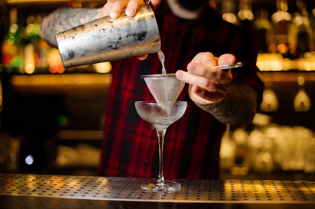 Barista che versa un cocktail reviver del corso dallo shaker in acciaio sul bancone del bar