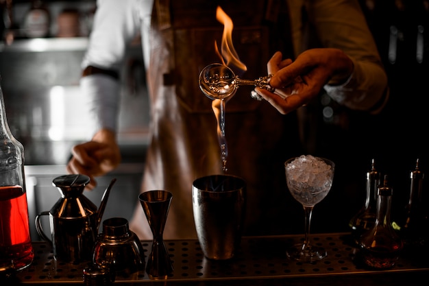 Bartender pouring an essence from the spoon in the flame to the steel shaker