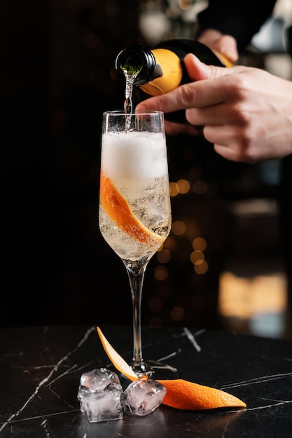 The bartender pouring sparkling wine into a glass with ice and orange zest