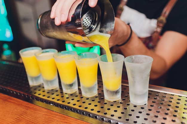 Bartender pouring strong alcoholic drink into small glasses on bar, shots.