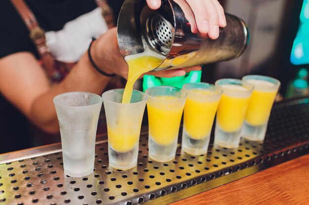 Foto barista che versa bevande alcoliche forti in piccoli bicchieri su bar