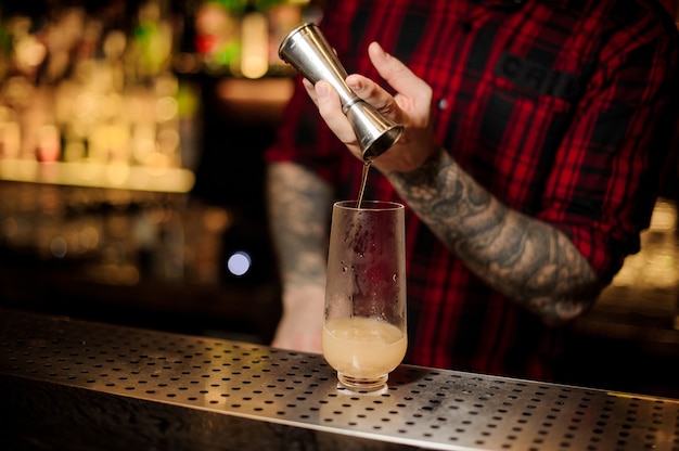 Barista che versa un cocktail trinidad swizzle dal jigger in acciaio al bicchiere sul bancone del bar