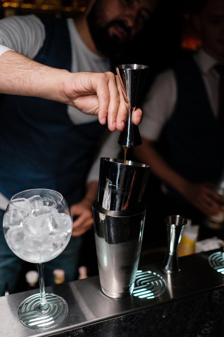 バーテンダーがメジャーカップからシェーカーにアルコールを注ぐ男性がバーでカクテルの作り方を学ぶ