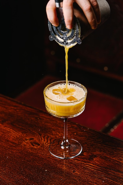The bartender pours an alcoholic cocktail with an orange on the table in the bar