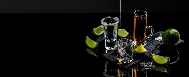 Il barista versa la tequila messicana con lime e sale su sfondo nero concetto bevanda di lusso bevanda alcolica congelare il movimento scende in spruzzi di liquido formato banner lungo