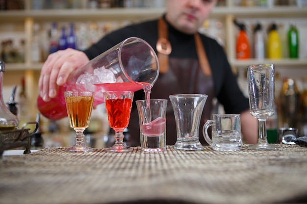 Bartender pours various of alcohol drink into small glasses on bar