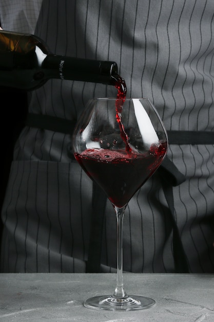 Bartender pours wine in glass on dark background