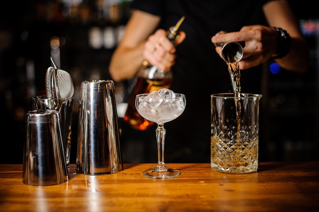 Foto il barista prepara un cocktail alcolico color ambra usando un bicchiere di cristallo con ghiaccio