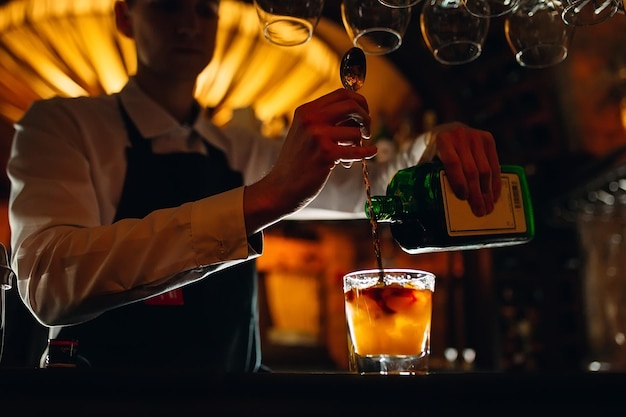 The bartender prepares a cocktail at the bar. The bartender pours alcohol from a bottle.