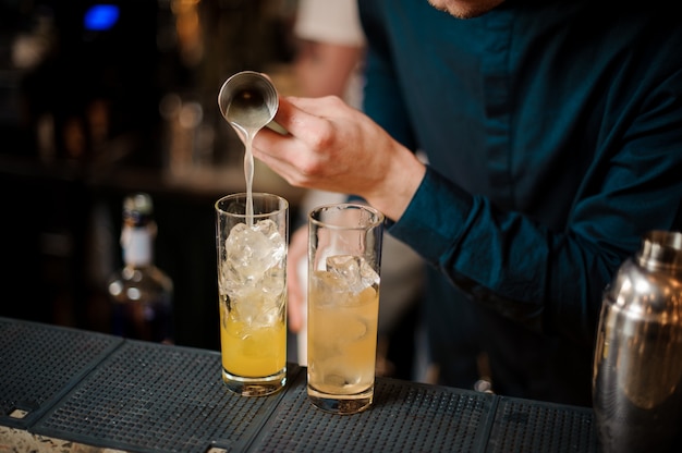Bartender prepares two alcoholic cocktails, adding an orange juice