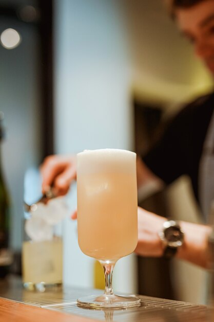 Bartender preparing gin and tonic with cucumber in the background, pina colada cocktail in the foreground. Photo with shallow depth of field. Vertical lifestyle image.