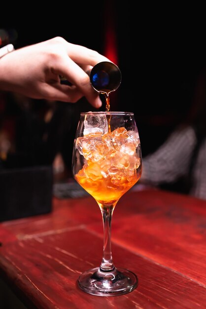 The bartender\'s hand pours an orange cocktail closeup a\
longstemmed glass in a club bar restaurant