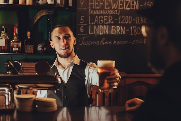 Bartender serves a glass of draft beer to male guest at bar