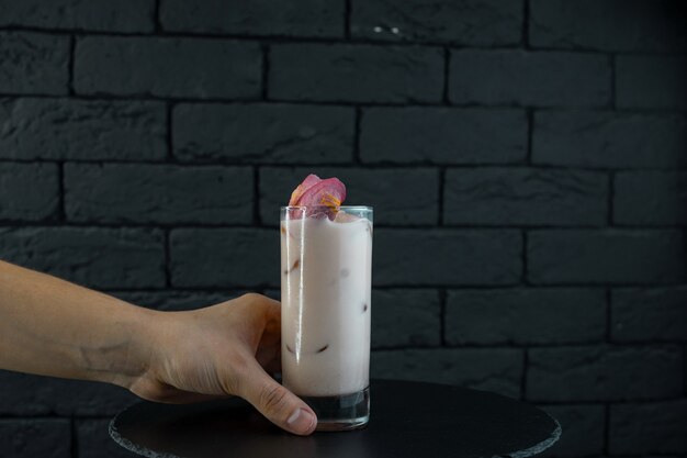 The bartender serves a sweet white milky alcoholic cocktail with strawberry juice with ice cubes, tonic and vodka on a black table in the bar. Alcoholic beverages. Night club life