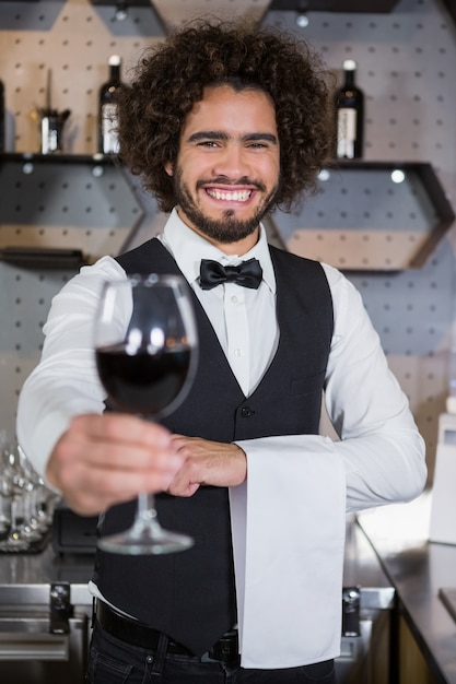 Bartender serving glass of red wine in bar counter