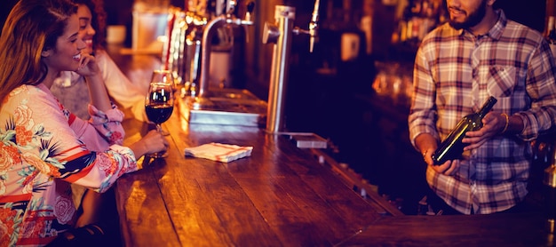 Photo bartender showing wine bottle to women at counter