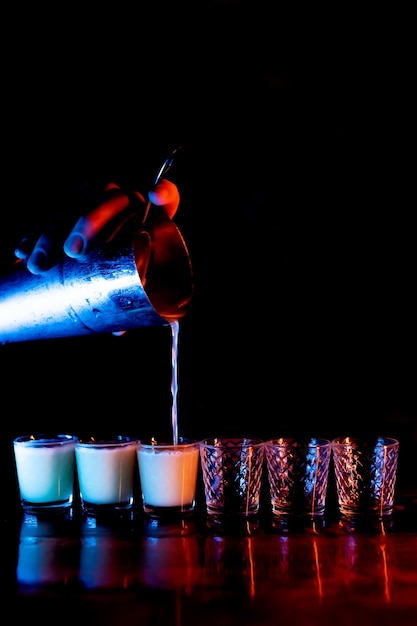 The bartender39s hand pours a mixed alcoholic cocktail from a shaker into shots Mixing alcohol cocktail in nightclub pub restaurant