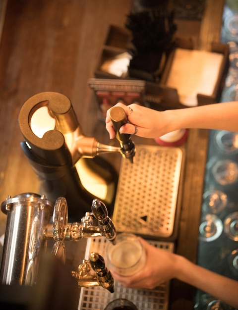 The bartenders hands pour beer from the tap