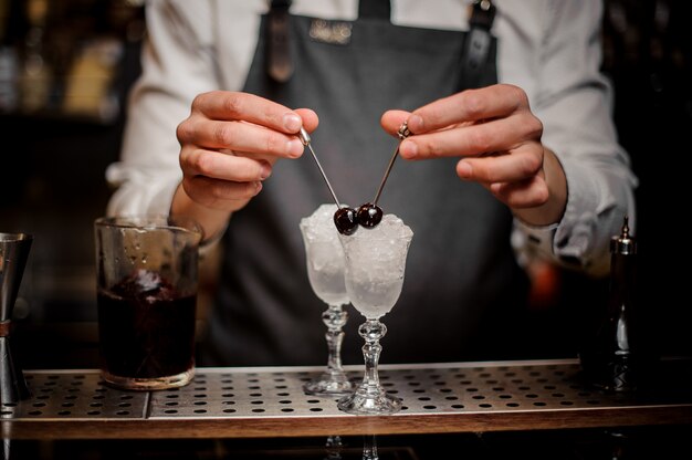 Foto bartman-handen versieren twee cocktailglazen met kersen