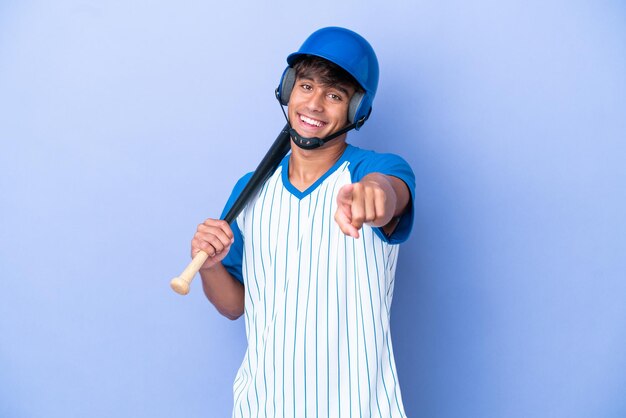 Baseball caucasian man player with helmet and bat isolated on blue background pointing front with happy expression