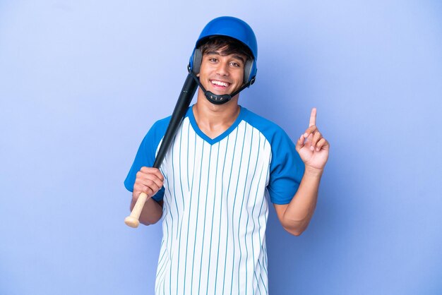 파란색 배경에 격리된 헬멧과 방망이를 가진 야구 백인 남자 선수는 최고의 표시로 손가락을 들고 들어올립니다.